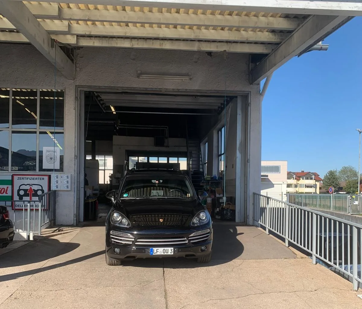 Porsche Cayenne fährt aus der CTC Werkstatt mit Prüfstellen-Schild